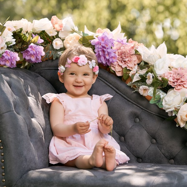 fotka maleho dievcatka s kvetinovou celenkou sediaceho na pohovke s kvetinovou girlandou